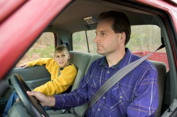 Young boy watching his dad drive from the passenger seat.