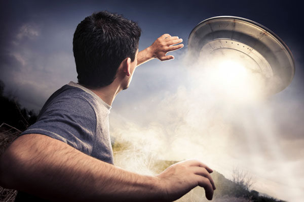 A man looking up at a UFO that is landing near him.
