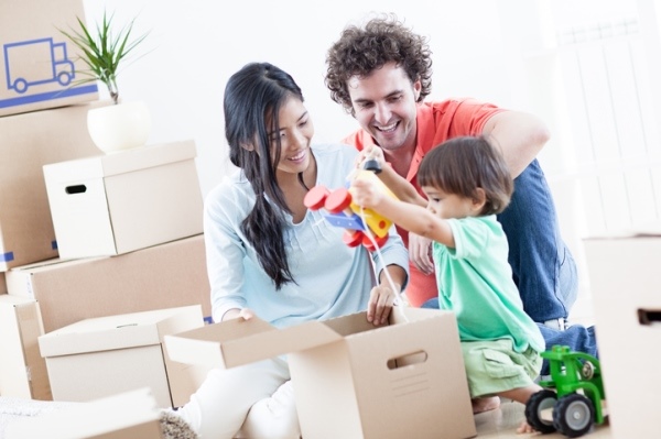 Young couple unpack moving boxes with their toddler who has just discovered a toy inside a box.