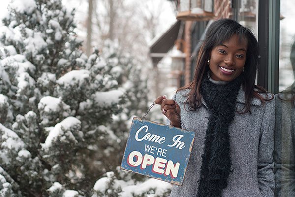 Business owner standing outside her shop with a welcome sign.
