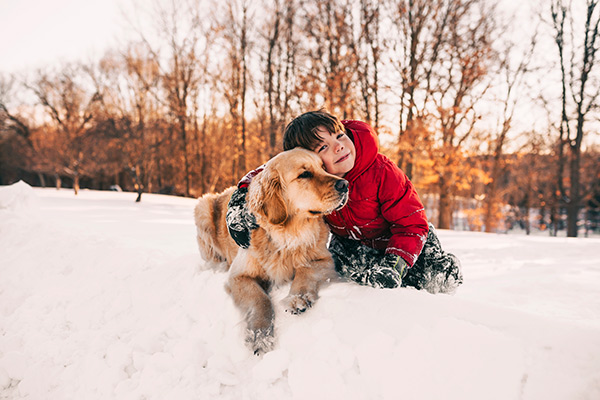 Young boy hugging his dog in his snow covered yard.