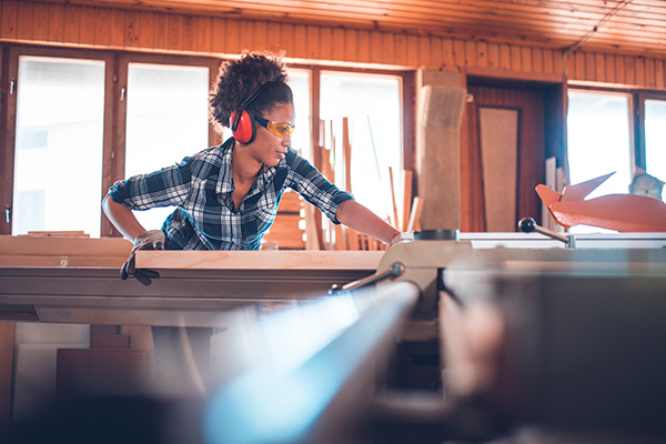 A woman using a table saw to cut wood.