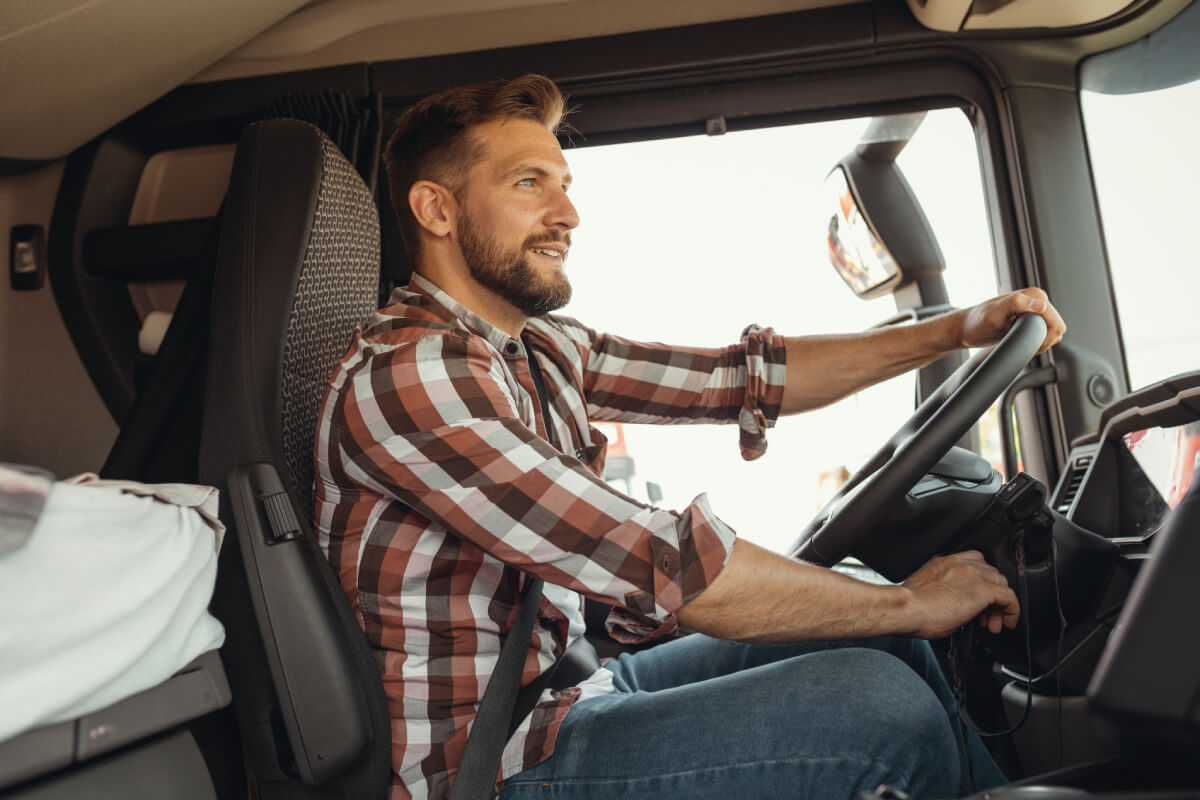 A smiling trucker driving his truck, to show insurance coverage for owner operators under permanent least to a motor carrier.