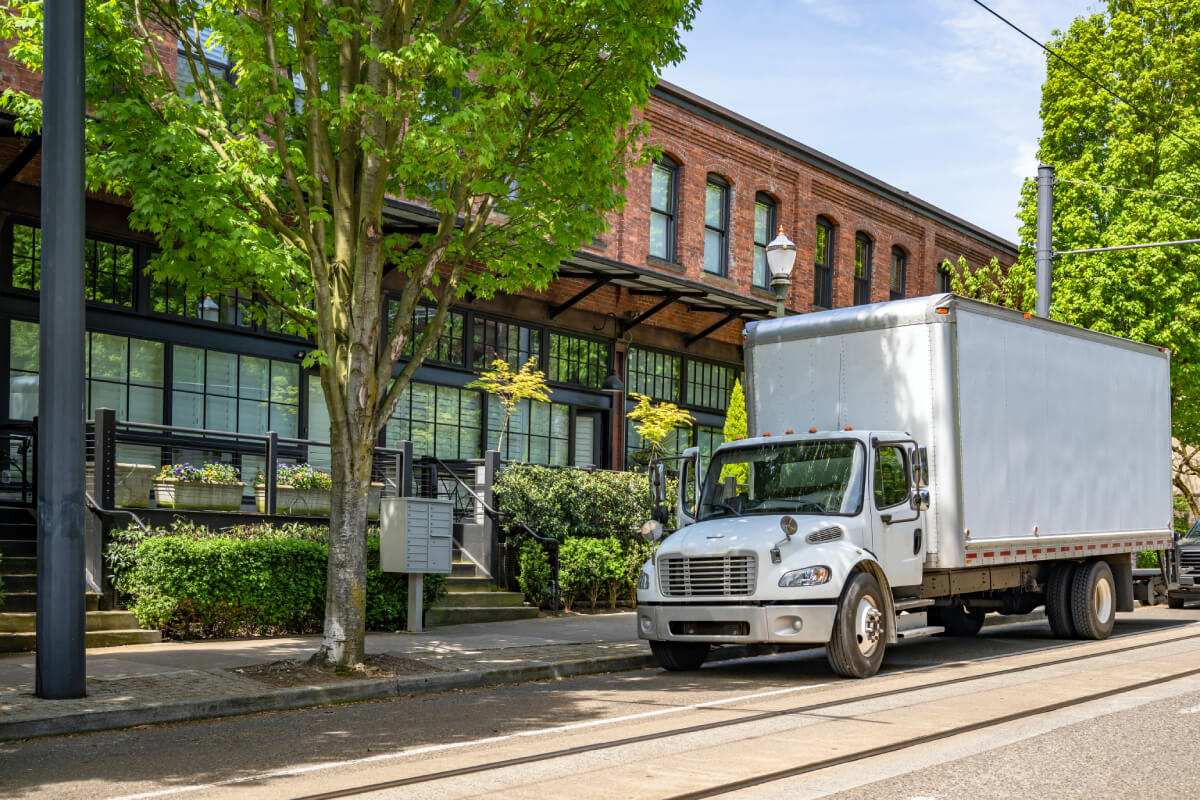 White box truck parked on the side of the street by an apartment building, used to illustrate that GEICO provides insurance coverage for various box truck types such as cargo cutaways, ice box trucks, and more.