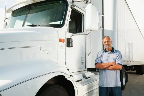 A truck driver with gray and blue uniform standing beside a semi-truck to symbolize the cost of truck insurance.