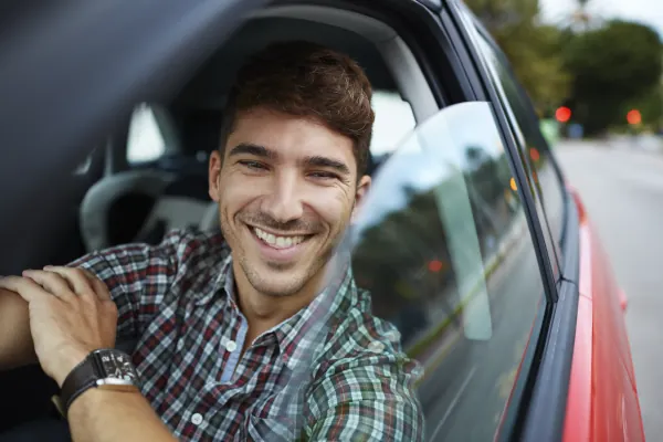 Close-up of a smiling driver in a parked car with city background, representing WY car insurance and reliable coverage.